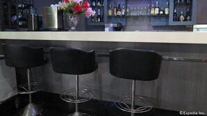 A bar area with three black bar stools, a metal bar counter, and shelves stocked with various liquor bottles. - Elegant Circle Inn (Cebu City)
