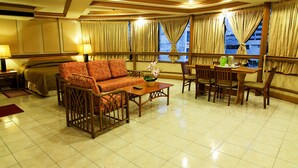 A hotel room with a sofa, dining table, chairs, a bed, and large windows with curtains. - Elegant Circle Inn (Cebu City)