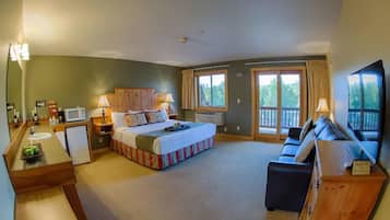 Habitación de hotel con cama, sofá, televisión, escritorio con lámpara, ventana y balcón.