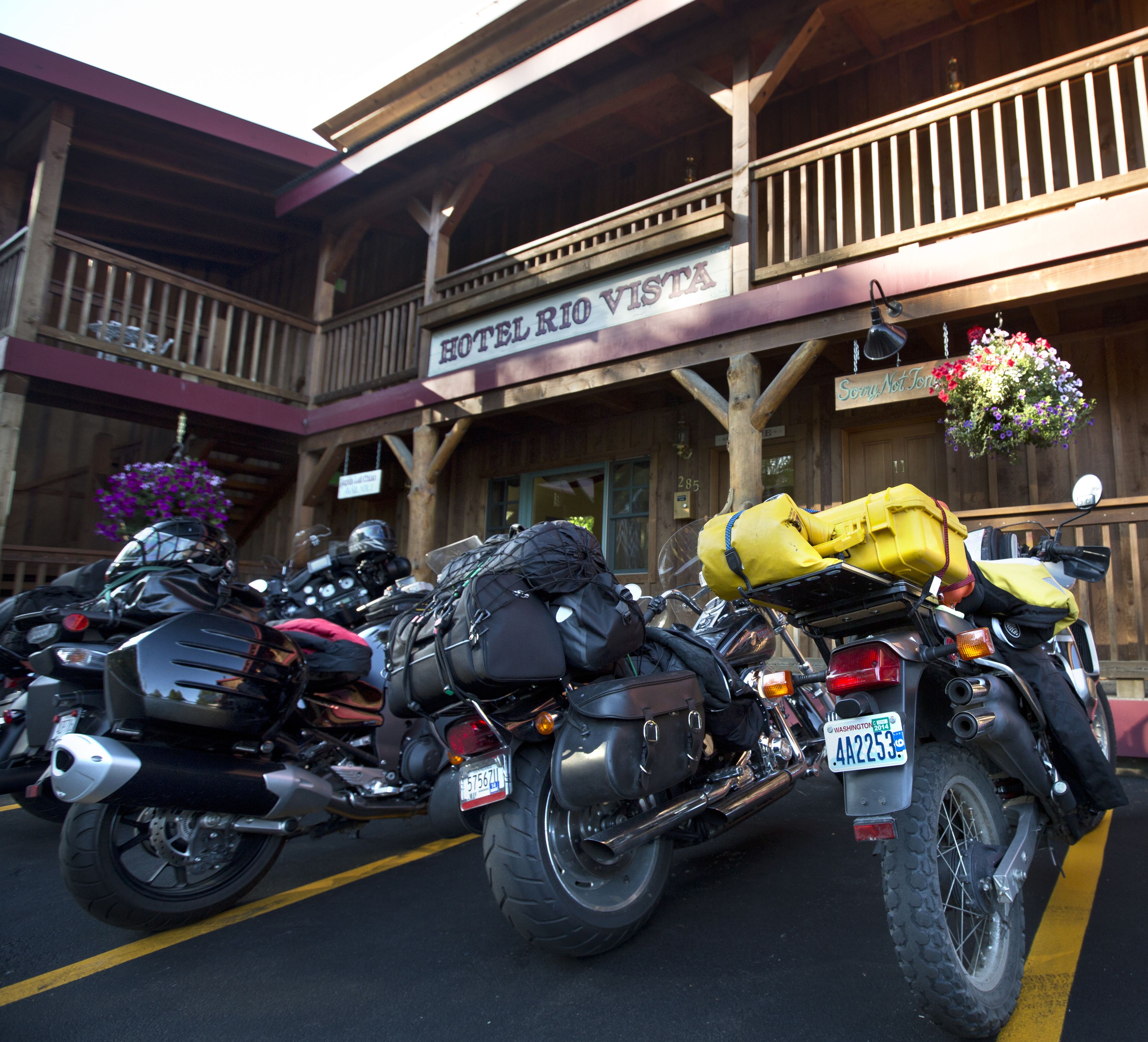 A row of motorcycles parked in front of a hotel with a wooden facade and a balcony.