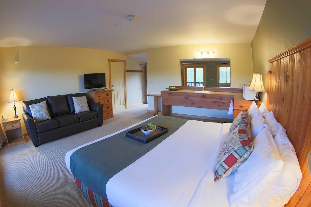 A hotel room with a bed, a sofa, a TV, a desk, and a mirror.