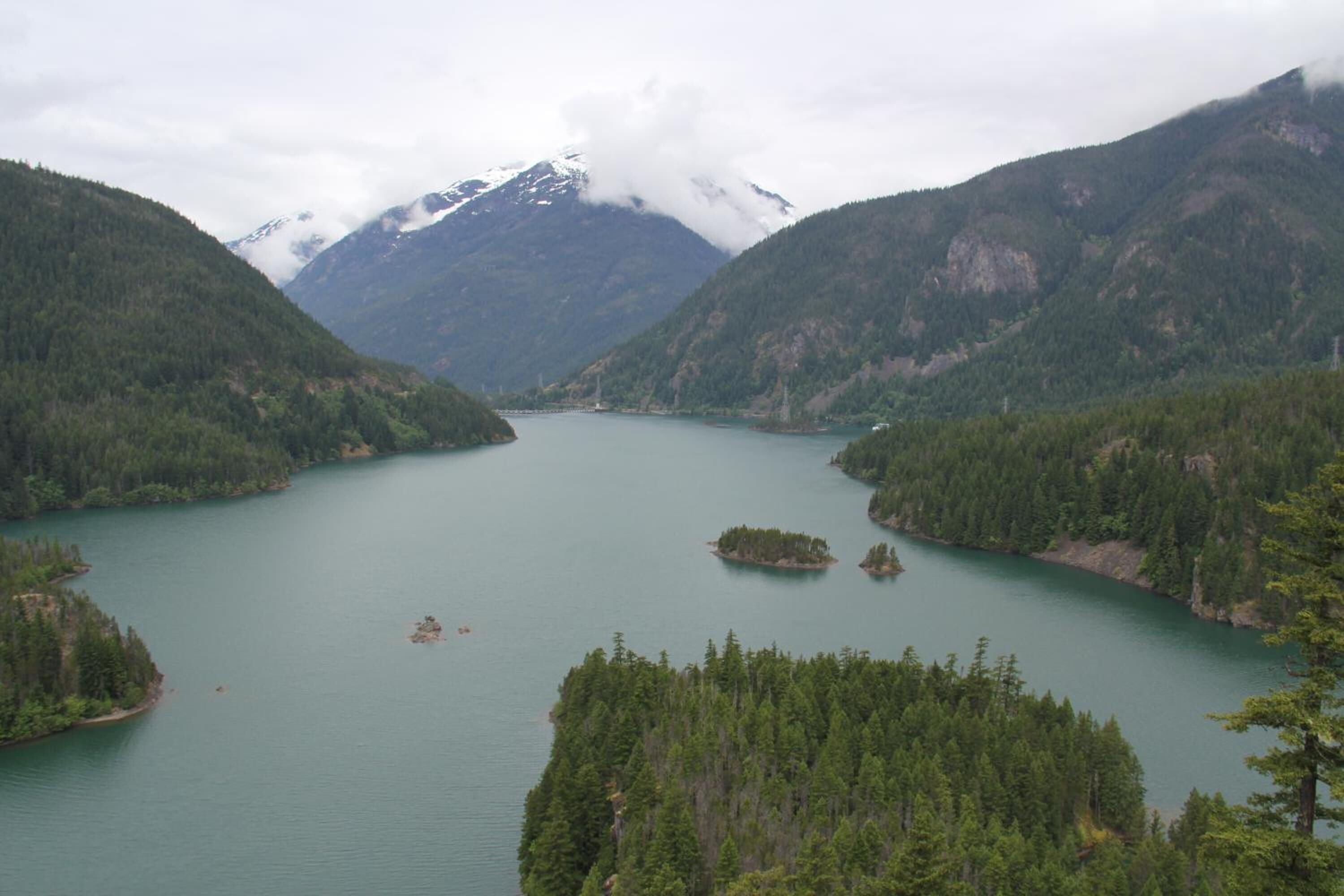 A lake surrounded by forested mountains with a cloudy sky.