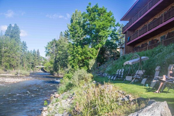 A riverside view with a building featuring balconies and outdoor seating.