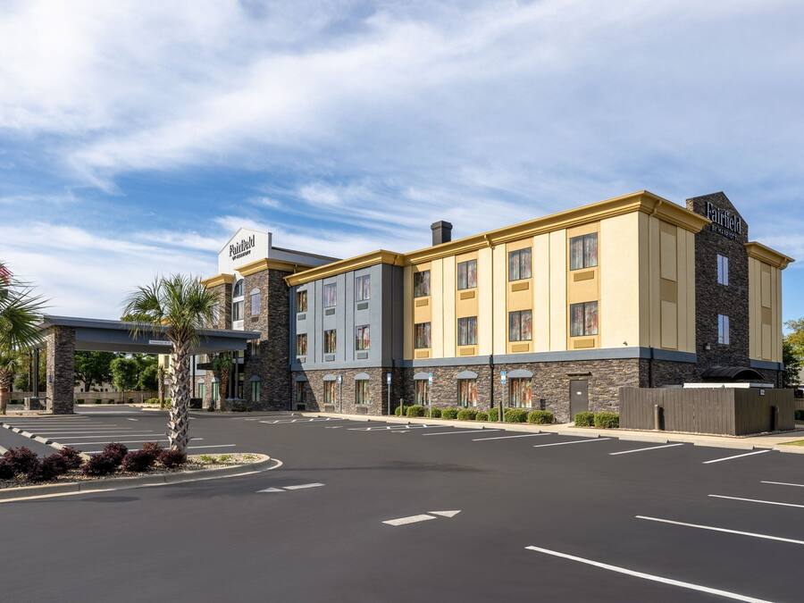 A multi-story hotel with a stone facade, a flat roof, and a parking lot with marked parking spaces.