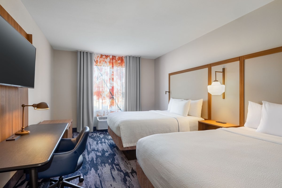 Une chambre d’hôtel avec deux lits, un bureau avec une chaise, un téléviseur à écran plat et une fenêtre avec des rideaux.