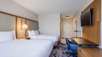 Quarto de hotel com duas camas, uma escrivaninha, uma cadeira, uma televisão e um abajur.