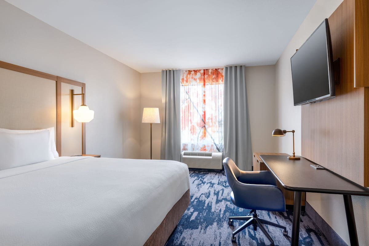 Une chambre d’hôtel avec un grand lit, un bureau, une chaise, une télévision et une fenêtre avec des rideaux.