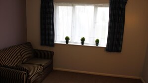 Una habitación con un sofá a rayas, una ventana con tres plantas en macetas y un piso alfombrado.