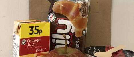A carton of orange juice, a bag of chocolate, a wooden spoon, and a container of assorted fruits.