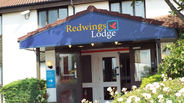 Exterior del Redwings Lodge con un toldo azul, una entrada accesible para sillas de ruedas y un letrero que indica un área de estacionamiento cercana.