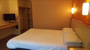 Habitación de hotel con una cama grande, un televisor sobre un mueble y una lámpara fijada a la pared.