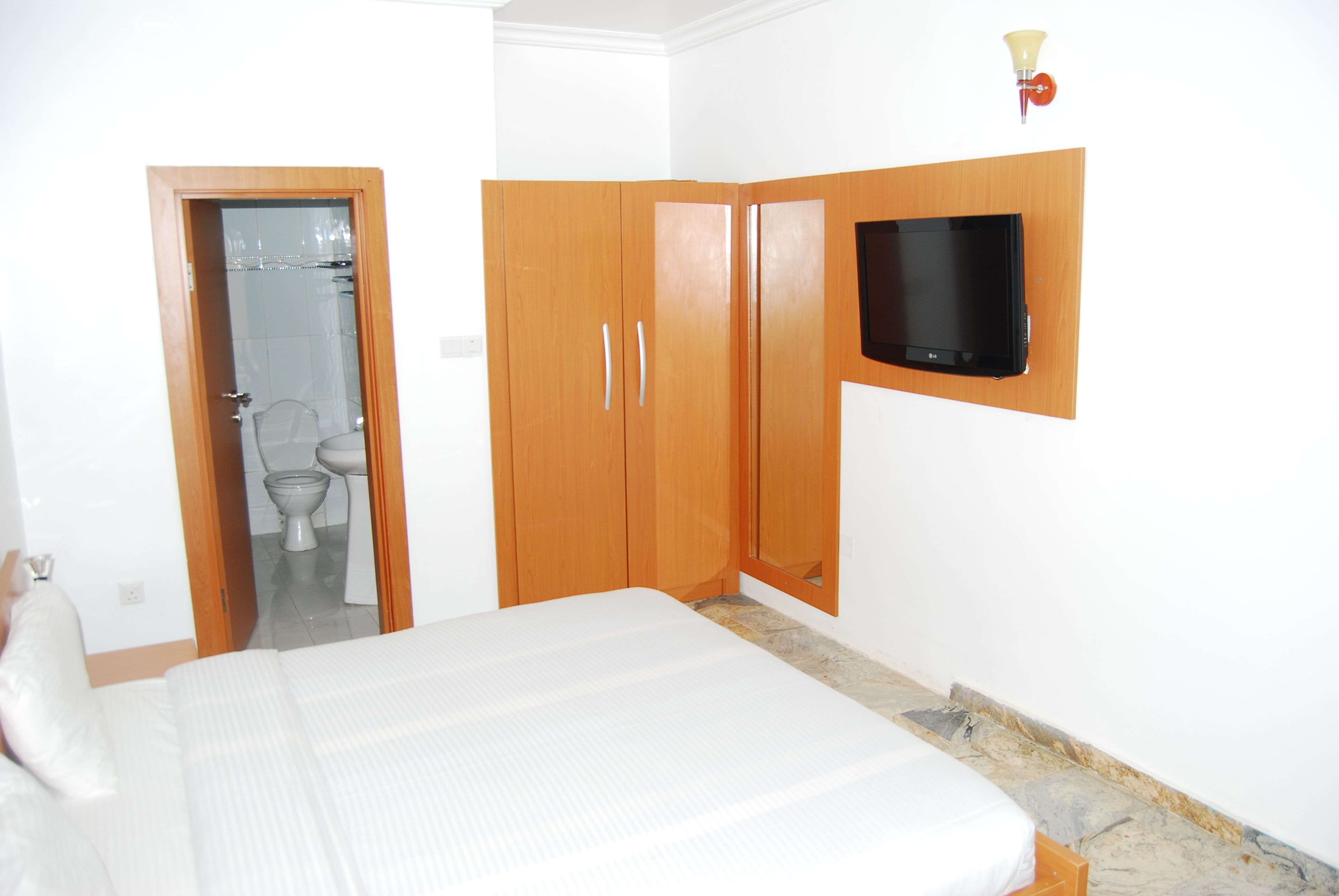 Un dormitorio con cama, armario de madera y televisor montado.