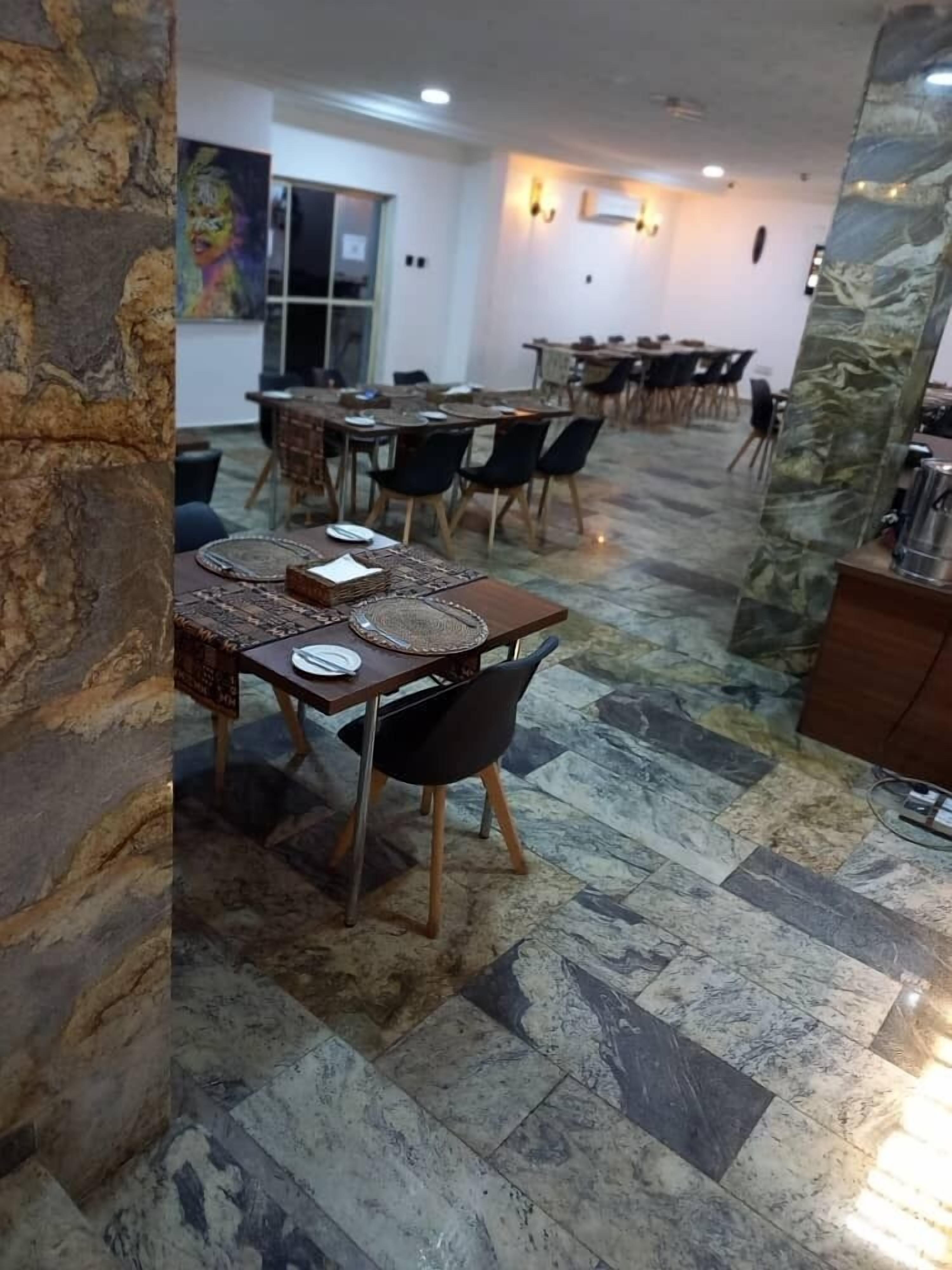 Un espace repas comprenant plusieurs tables et chaises, des colonnes en pierre et un sol carrelé.