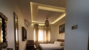 A hotel room with a large bed, a wooden dining table, a chandelier, and a view of the city through the window. - 3J's Hotels & Apartments (Abuja)