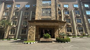 A multi-story building with a central entrance, air conditioning units, and a parking lot. - 3J's Hotels & Apartments (Abuja)
