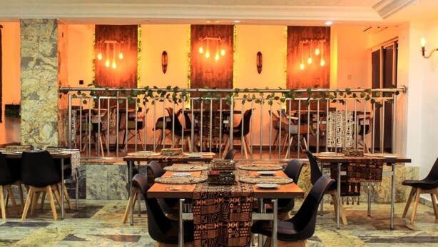 A restaurant with multiple tables, chairs, and a decorative wall with hanging lights. - 3J's Hotels & Apartments (Abuja)
