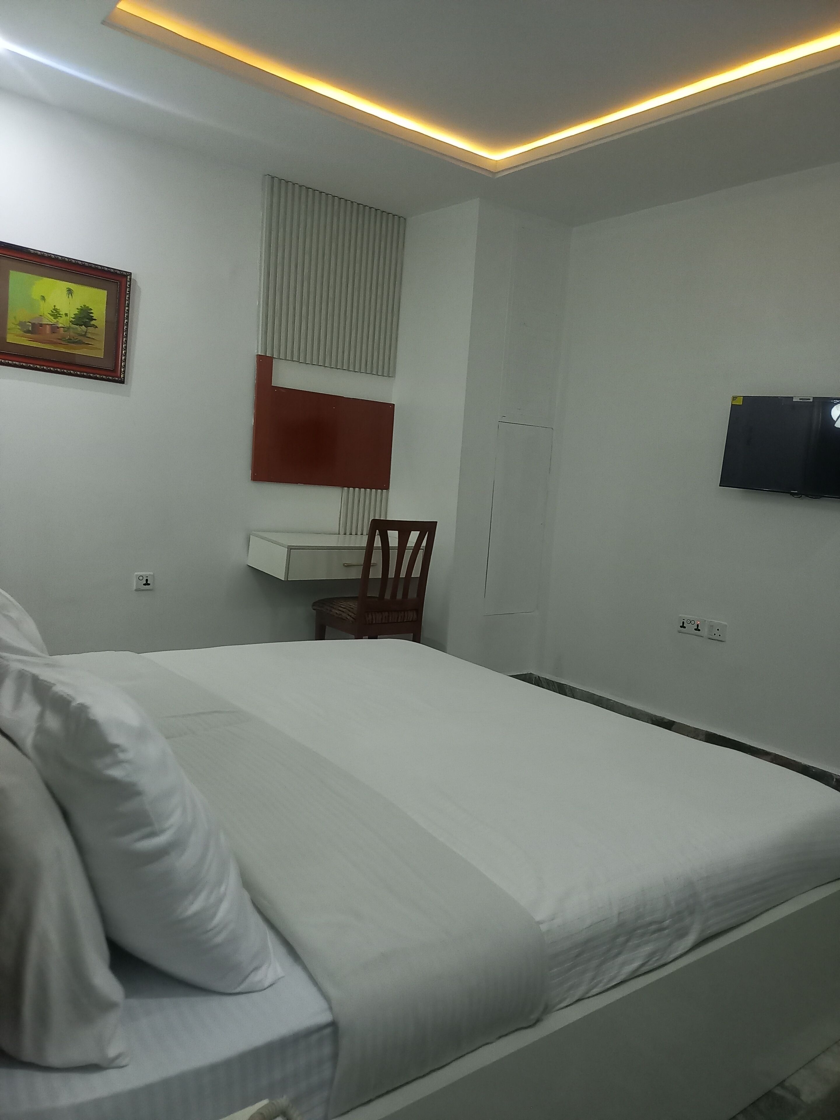 A hotel room with a bed, a desk, a chair, a television, and a painting on the wall.