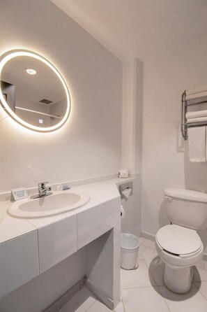 Un baño moderno con lavamanos, espejo y retrete blancos.