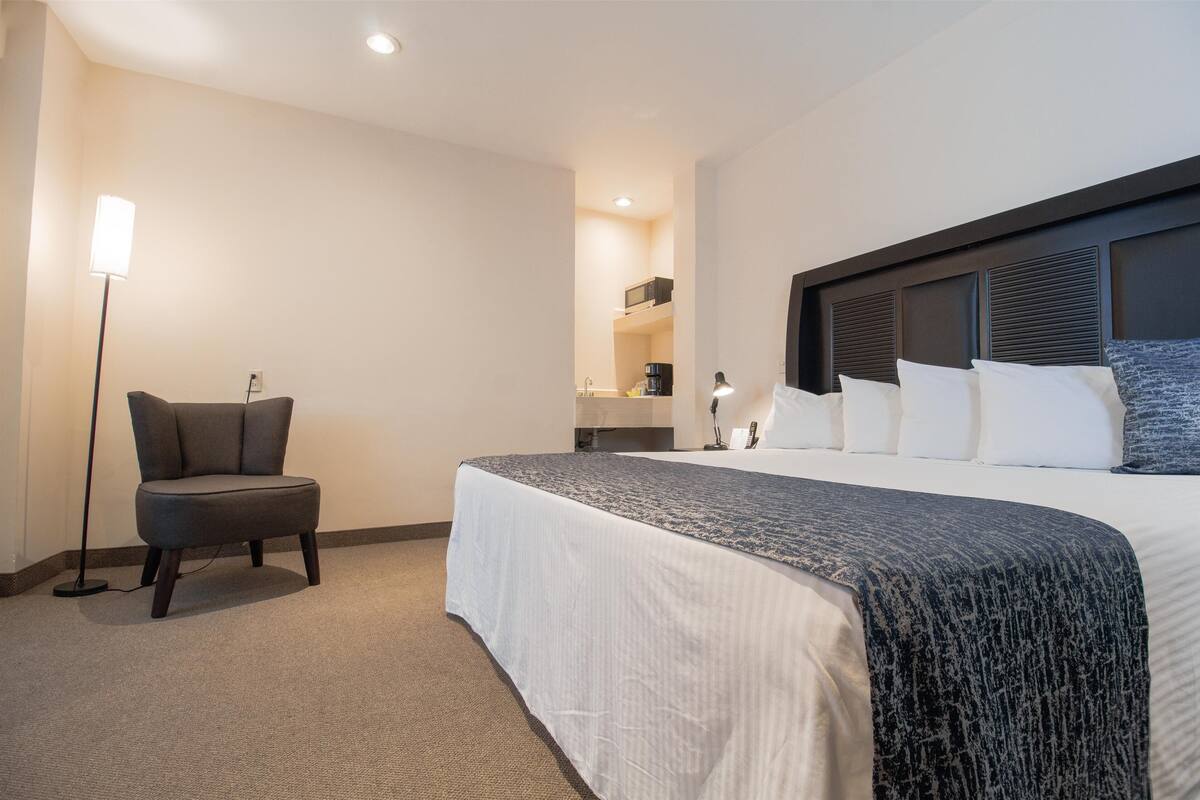 A hotel room with a large bed, a chair, a desk, and a lamp.