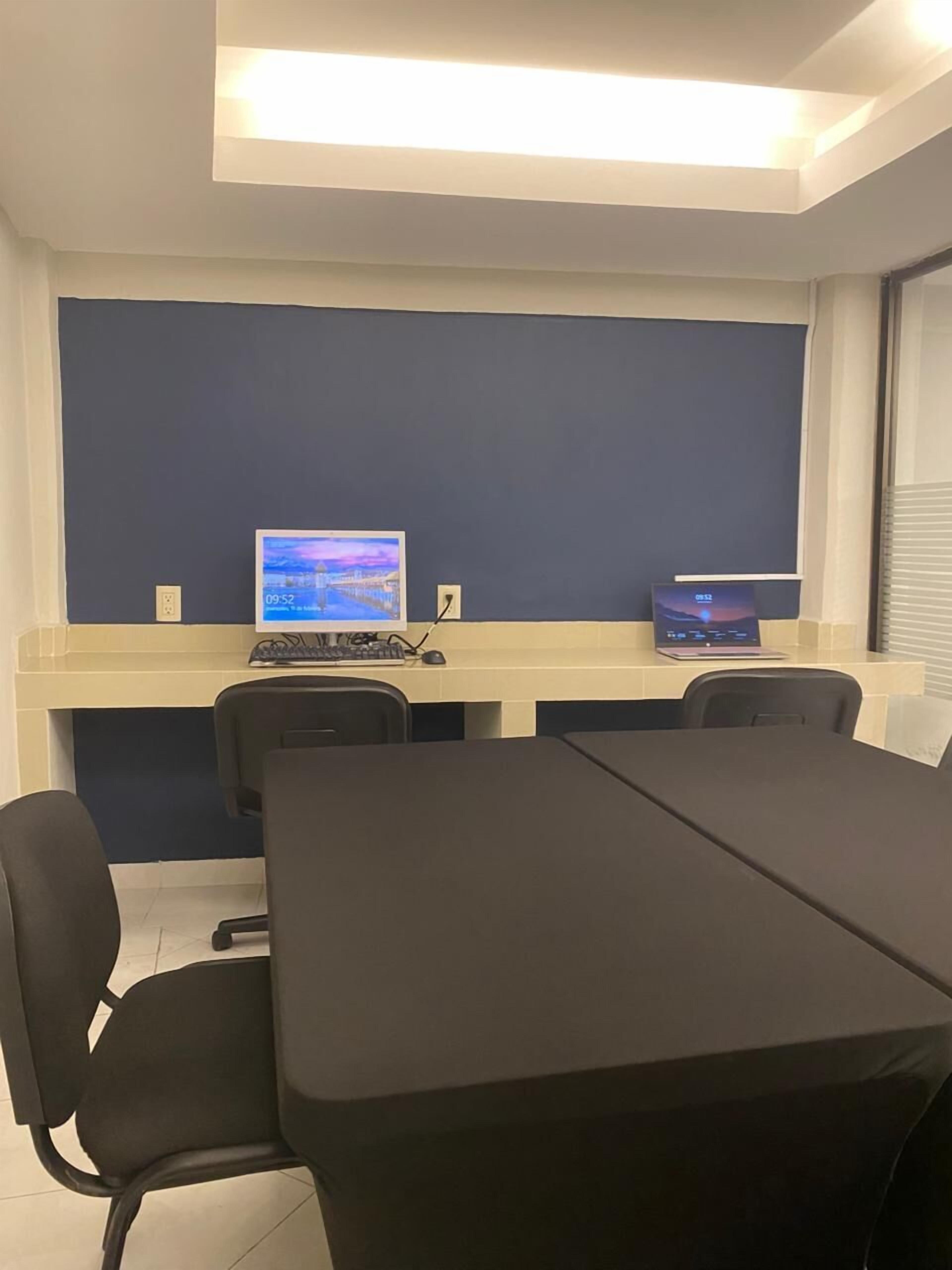 Una sala conferenze con un lungo tavolo, due monitor per computer e sedie da ufficio nere.