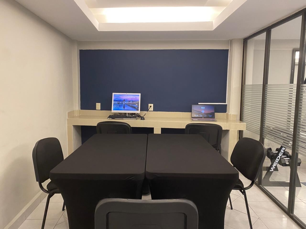 A conference room with a long table, four chairs, two computers, and a large window with blinds.