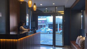 A modern hotel reception area with a wooden reception desk, pendant lighting, and a view of the street outside. - Best Western Real Tula Express (Tula de Allende)