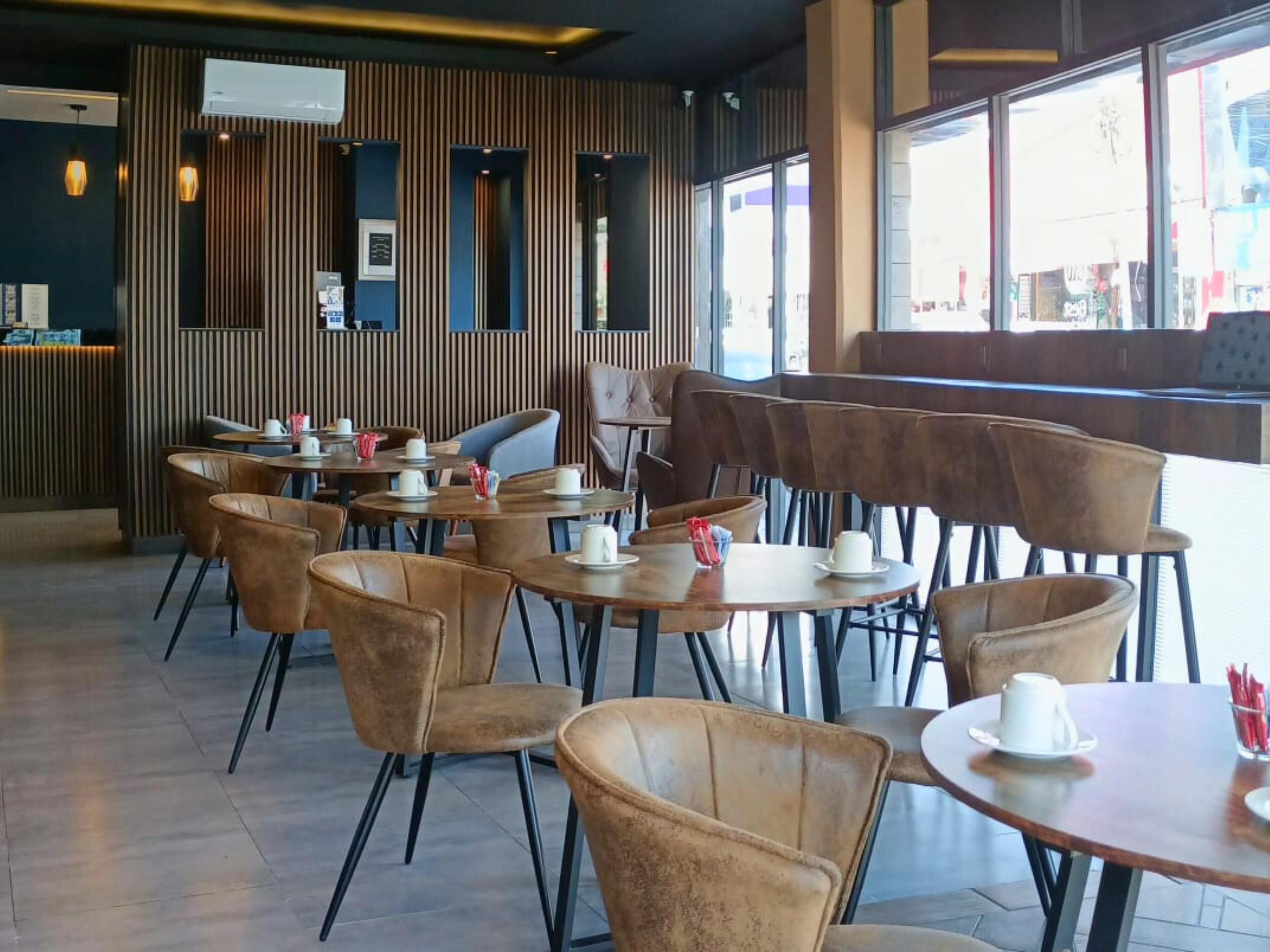 Ein modernes Café mit Holzwänden, Ledersesseln und Tischen, die mit weißen Tassen und Untertassen gedeckt sind.