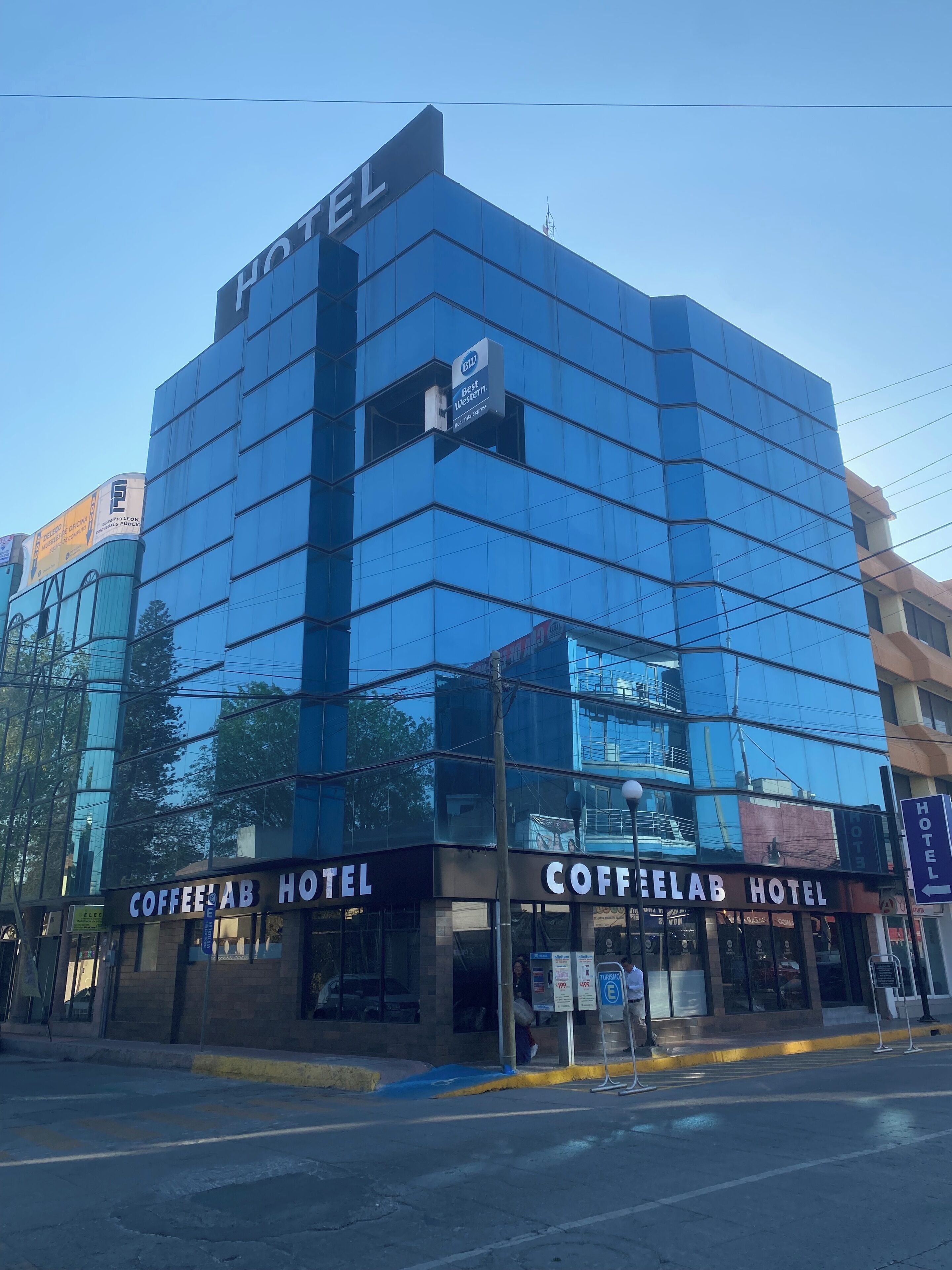 Un hotel moderno con fachada de vidrio, llamado "COFFEE LAB HOTEL", que presenta un letrero llamativo y una pequeña ventana con un cartel encima.