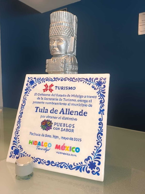 Una placa con una estatua de Buda de plata en la parte superior, que presenta texto sobre el turismo en Hidalgo, México, y una fecha para un evento en mayo de 2025.