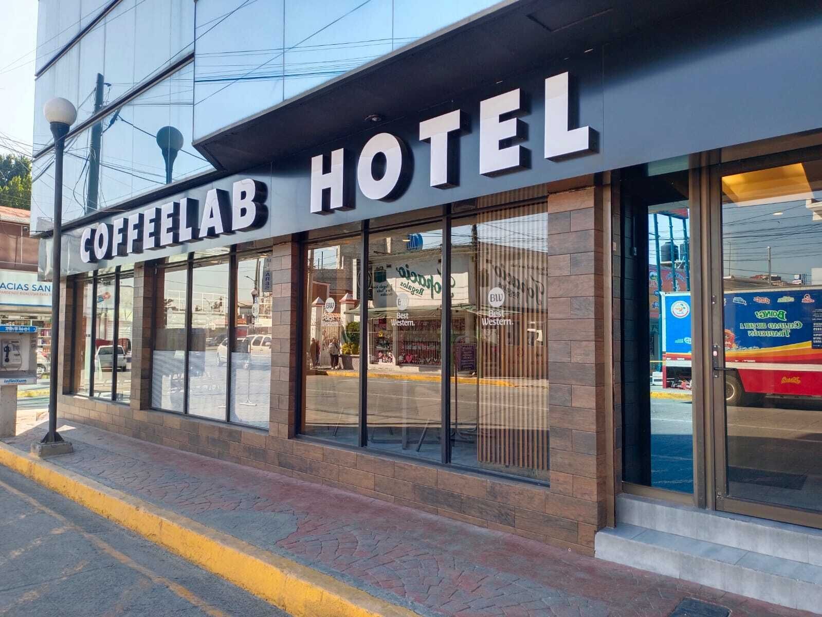 Un hotel llamado "COFFEELAB HOTEL" con gran cartelera, fachada moderna y amplios ventanales.