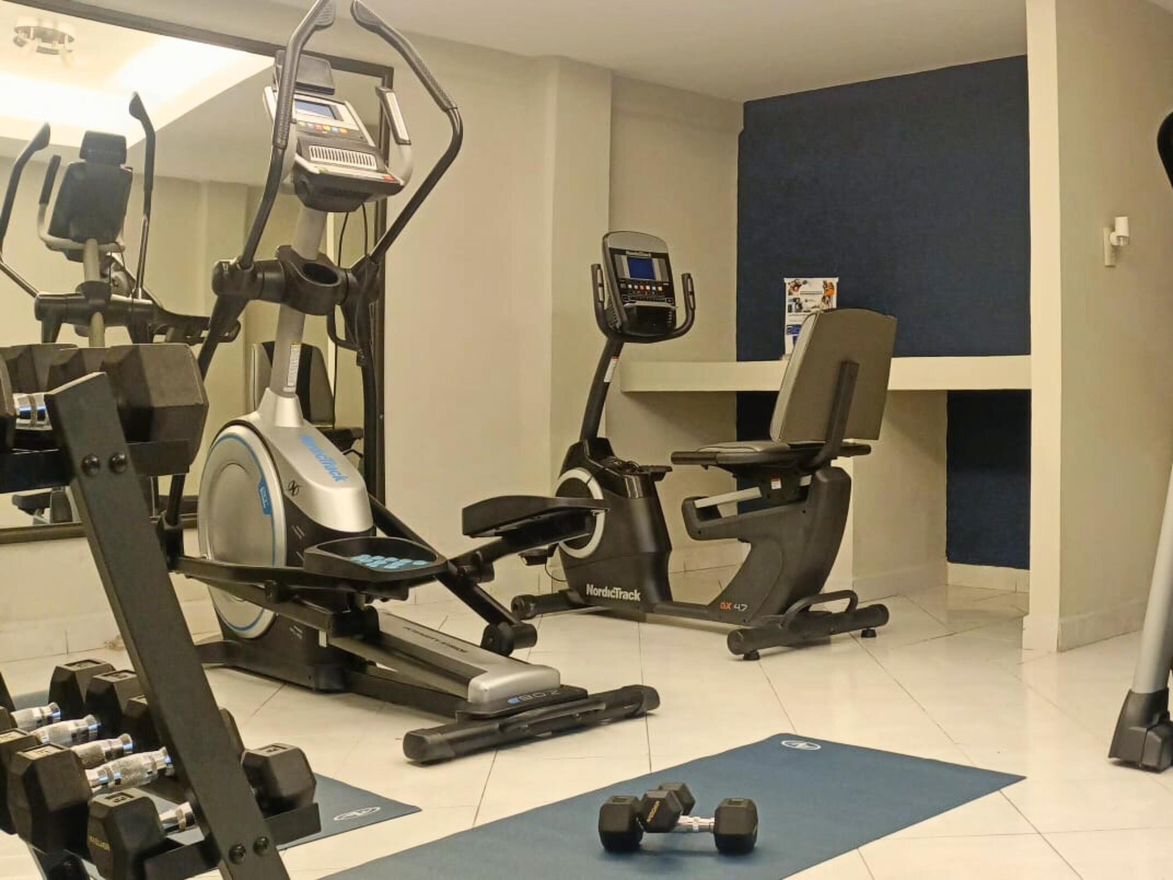 A gym with cardio machines, dumbbells, and a blue mat.