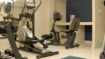A gym with cardio machines, dumbbells, and a blue mat.