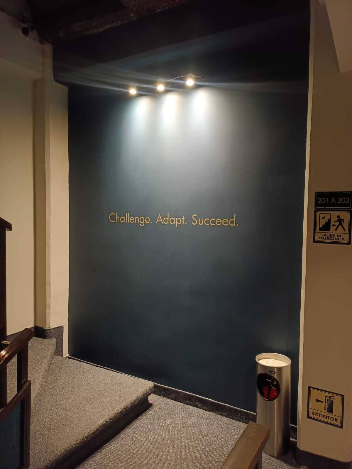 A staircase with a motivational quote on the wall, a fire extinguisher, and emergency exit signs.