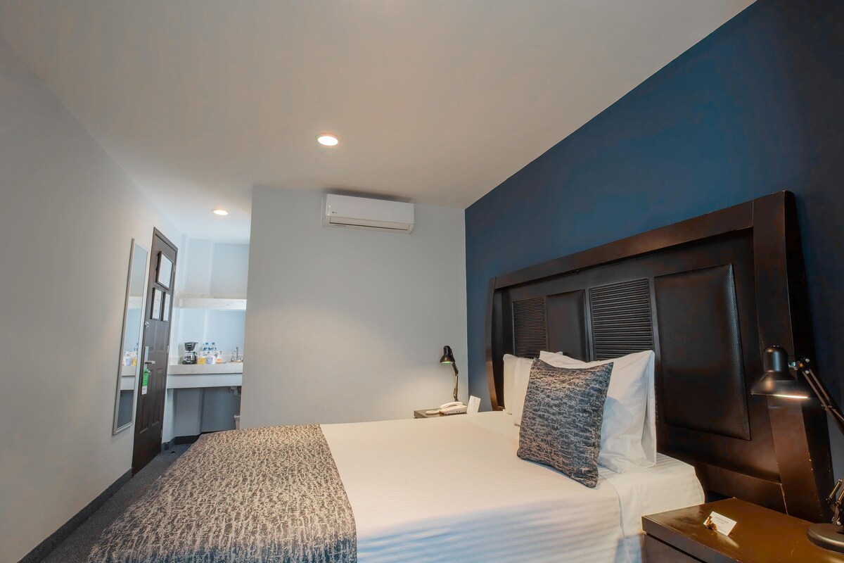Habitación de hotel con cama, lámpara de noche y vista al baño.