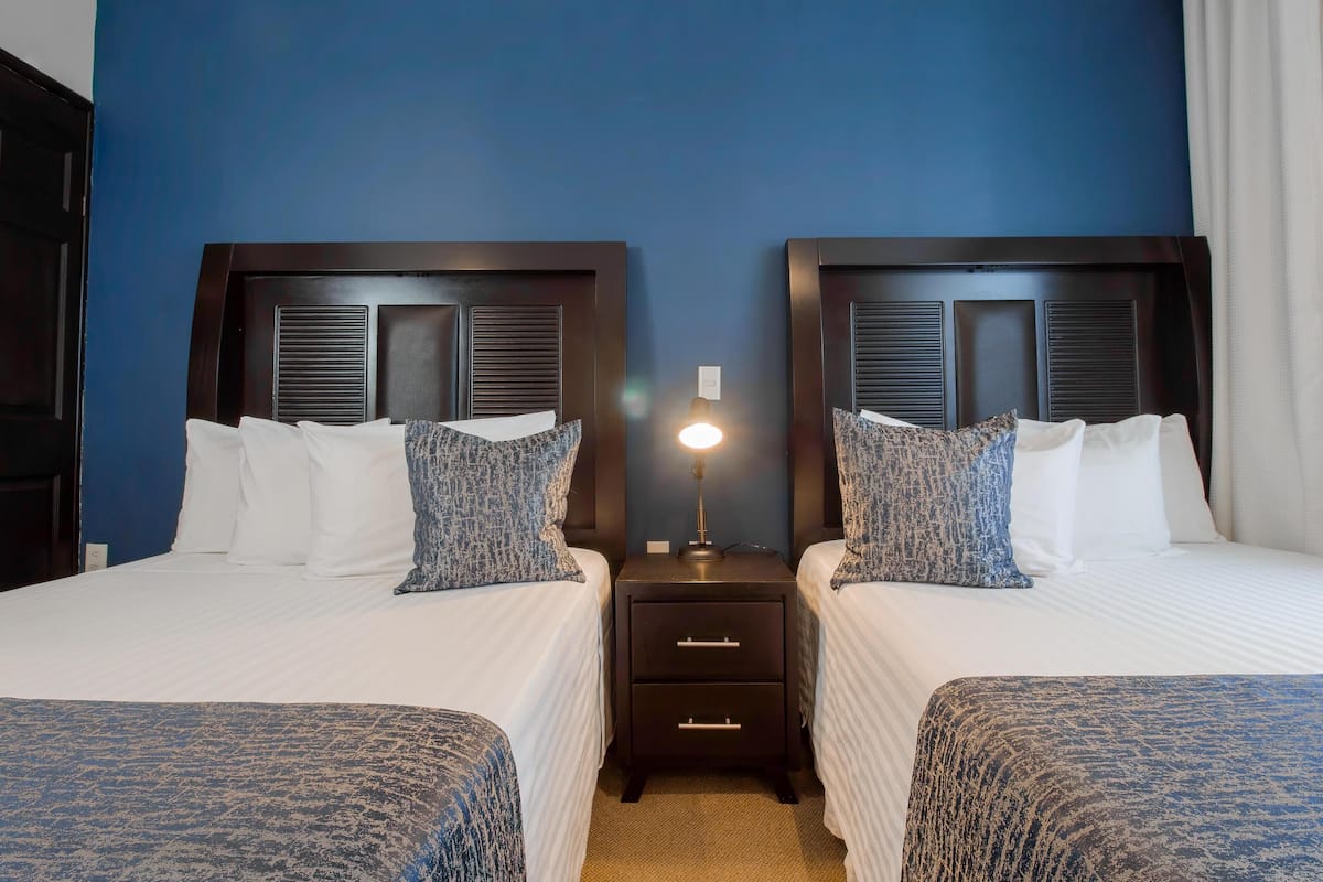 A hotel room with two beds, a nightstand with a lamp, and a dark wooden headboard.