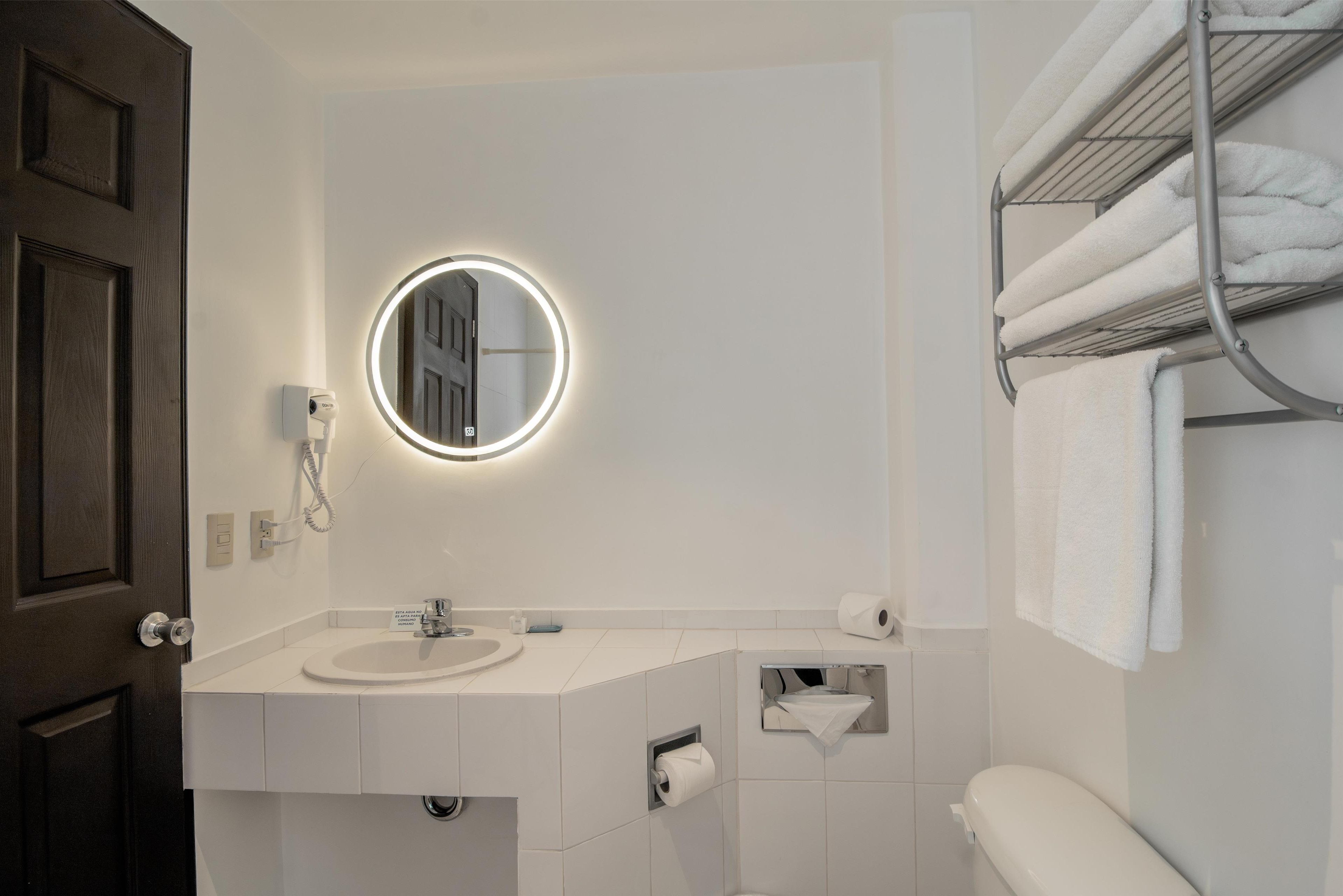 Un baño moderno con espejo redondo, lavabo blanco y toallero.