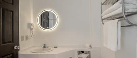 Un baño moderno con espejo redondo, lavabo blanco y toallero.