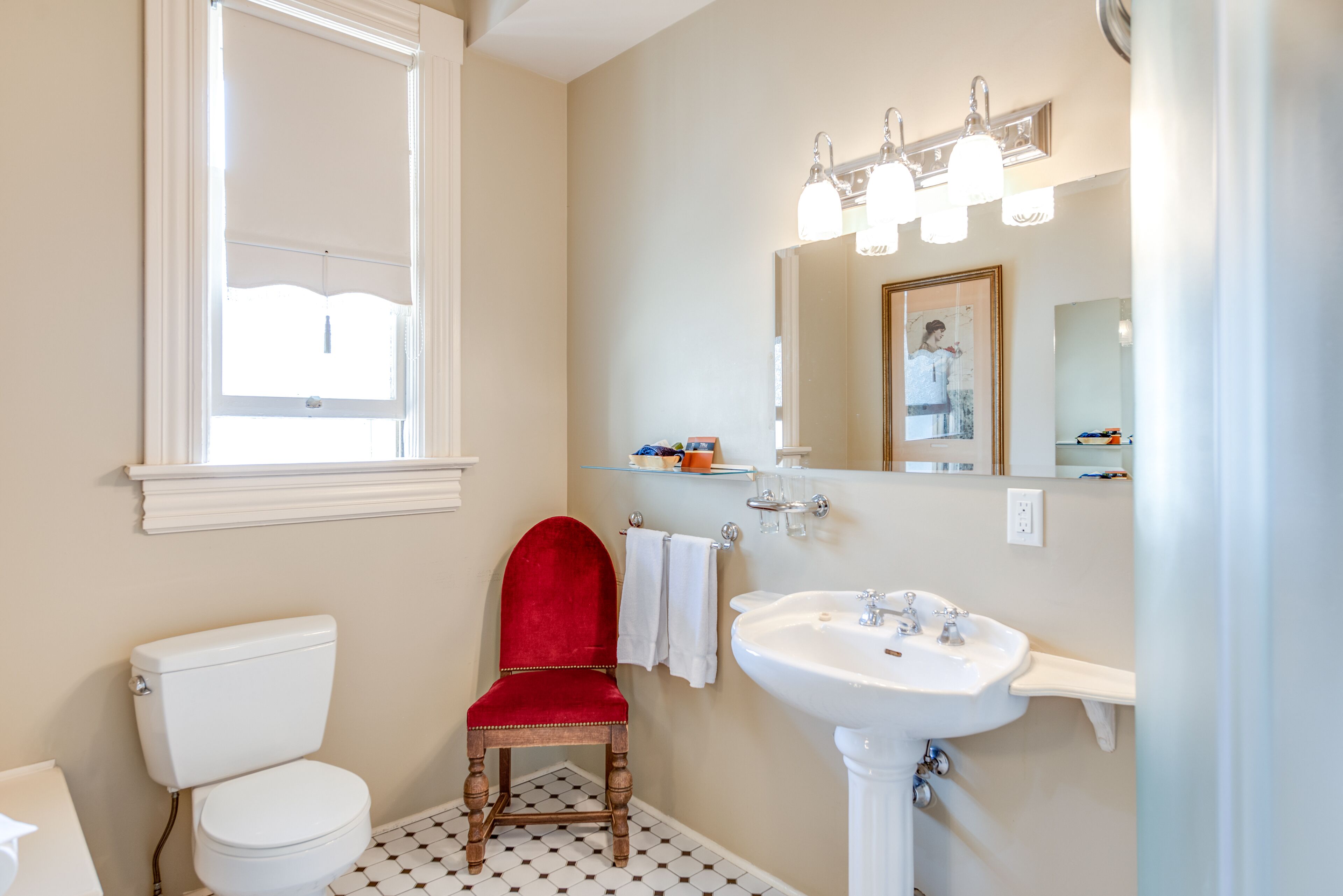 Ein Badezimmer mit Toilette, einem roten Stuhl, einem Waschbecken und einem Spiegel.