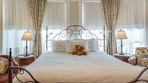 A bedroom with a large bed, two bedside lamps, a floral armchair, and a teddy bear on the bed. - O Canada House (Vancouver)