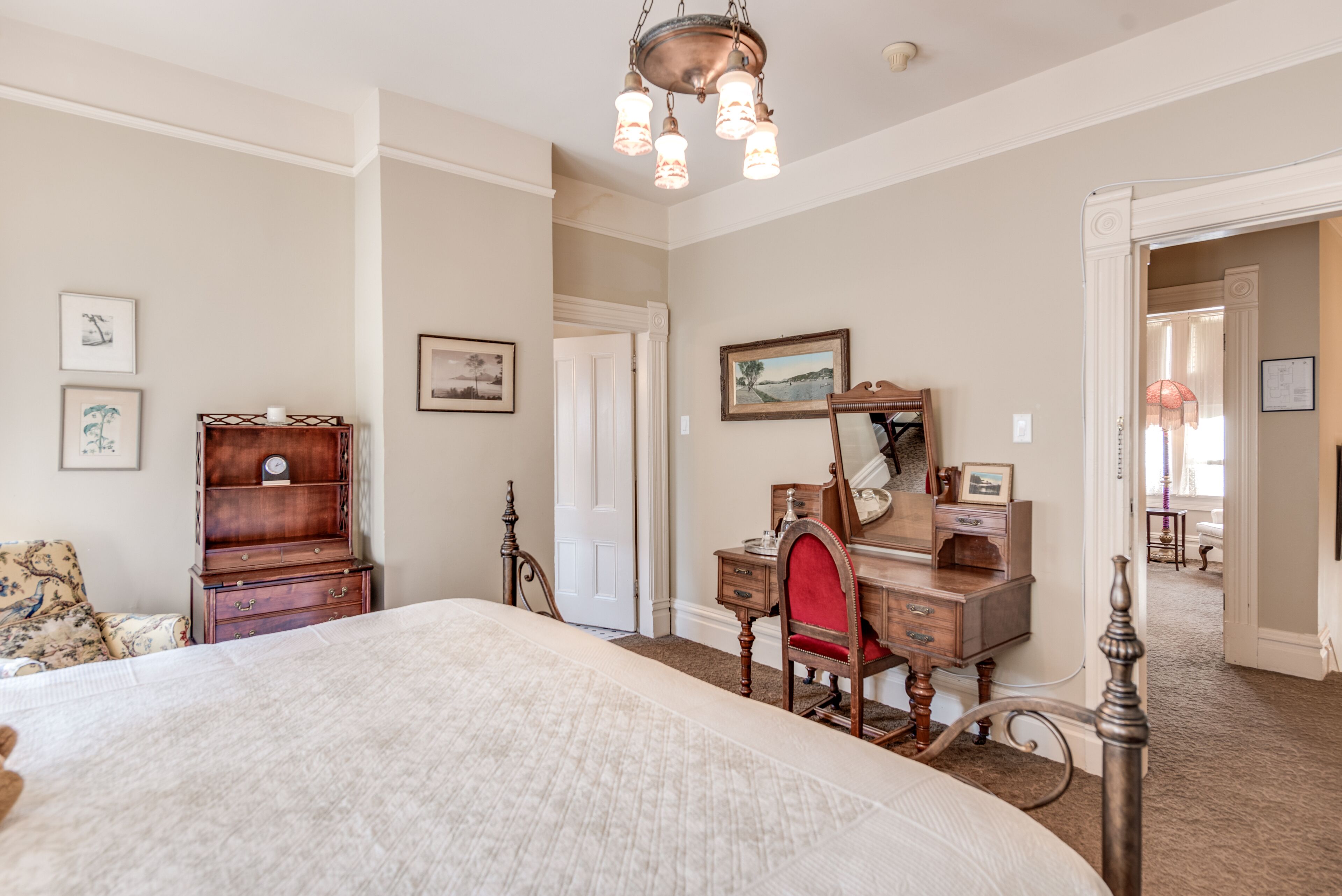 Une chambre à coucher avec un grand lit, une commode en bois, un miroir et une porte donnant sur une autre pièce.