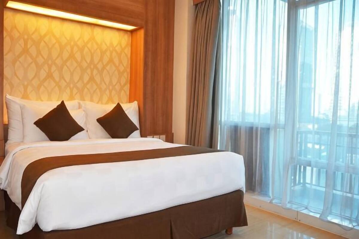 A hotel room with a large bed, a window with curtains, and a view of the outside.