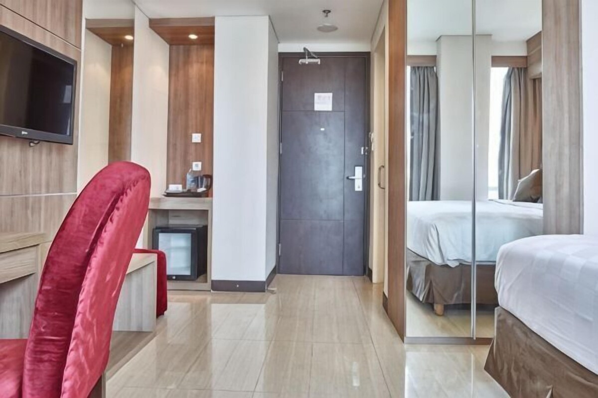 Une chambre d’hôtel avec un lit, un bureau et une chaise, une télévision et une porte.