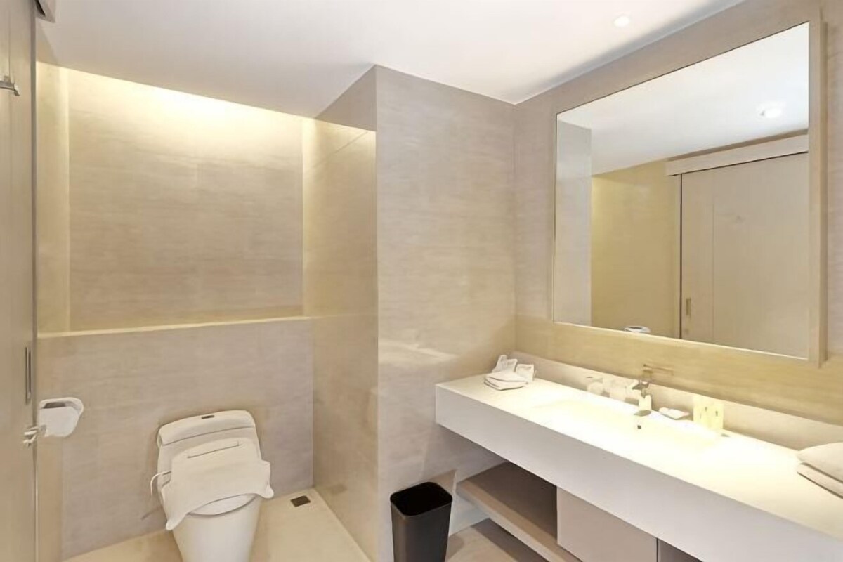 A modern bathroom with a large mirror, a white sink, and a shower area.
