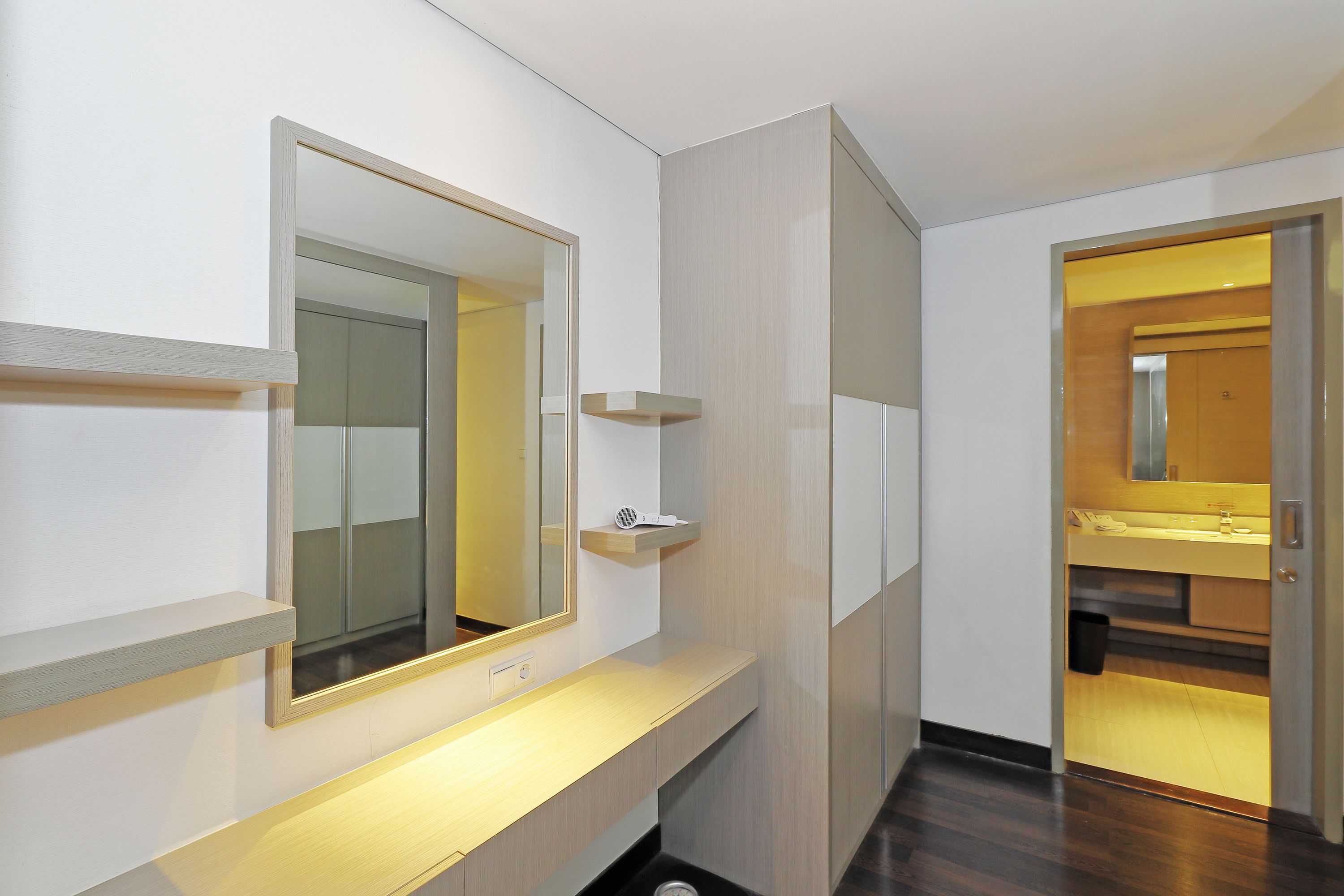 A modern bathroom with a large mirror, a vanity with a lighted countertop, and a wooden floor.
