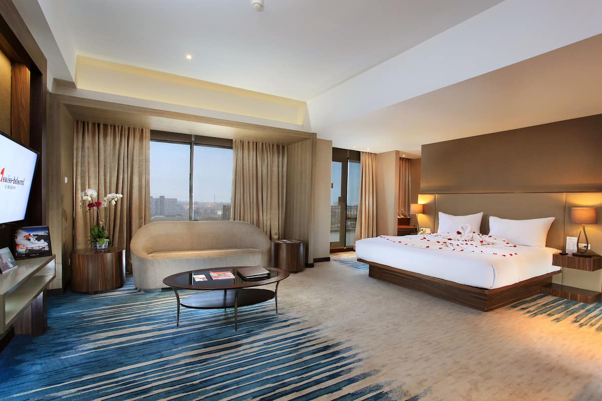 Una habitación de hotel con una cama grande, un sofá, una mesita de café y un televisor.