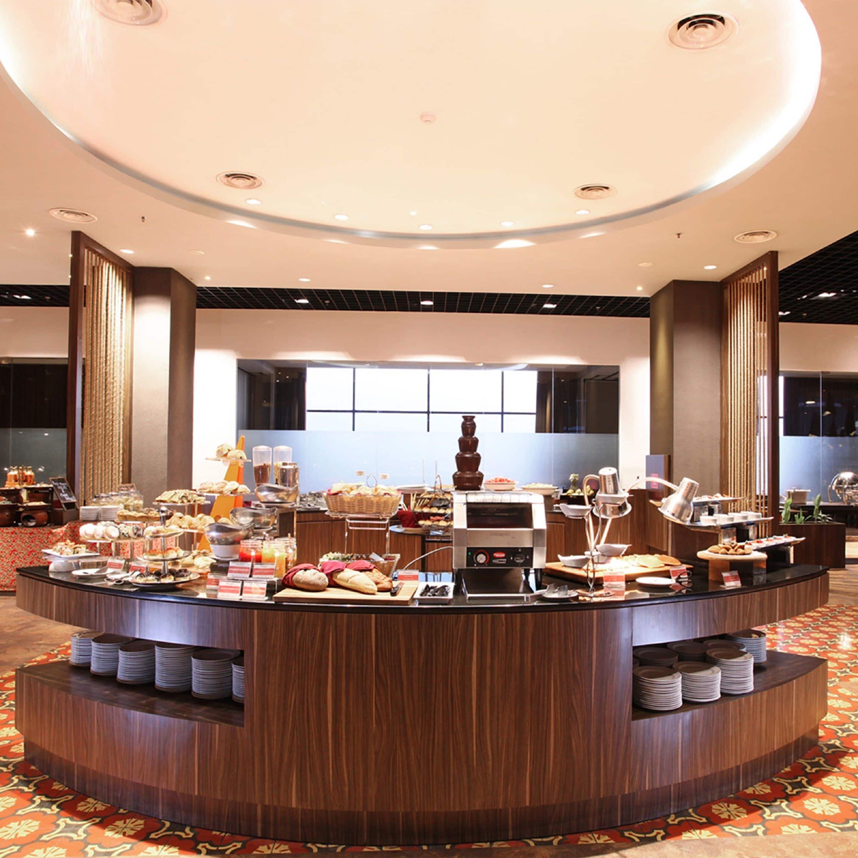 A buffet setup with various food items and a coffee machine, surrounded by a circular counter and a patterned carpet.