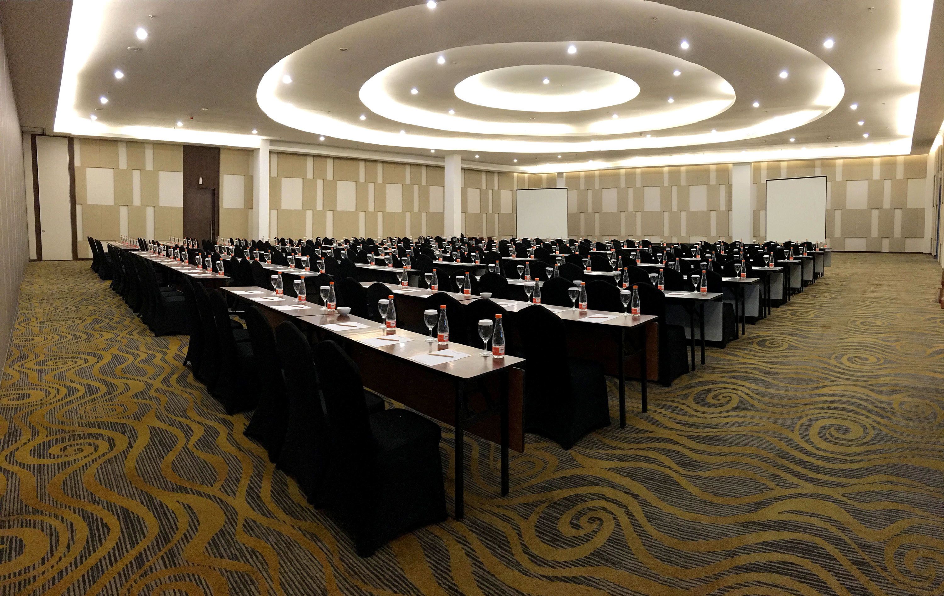 Un salón de conferencias con varias mesas, sillas y una pantalla grande.