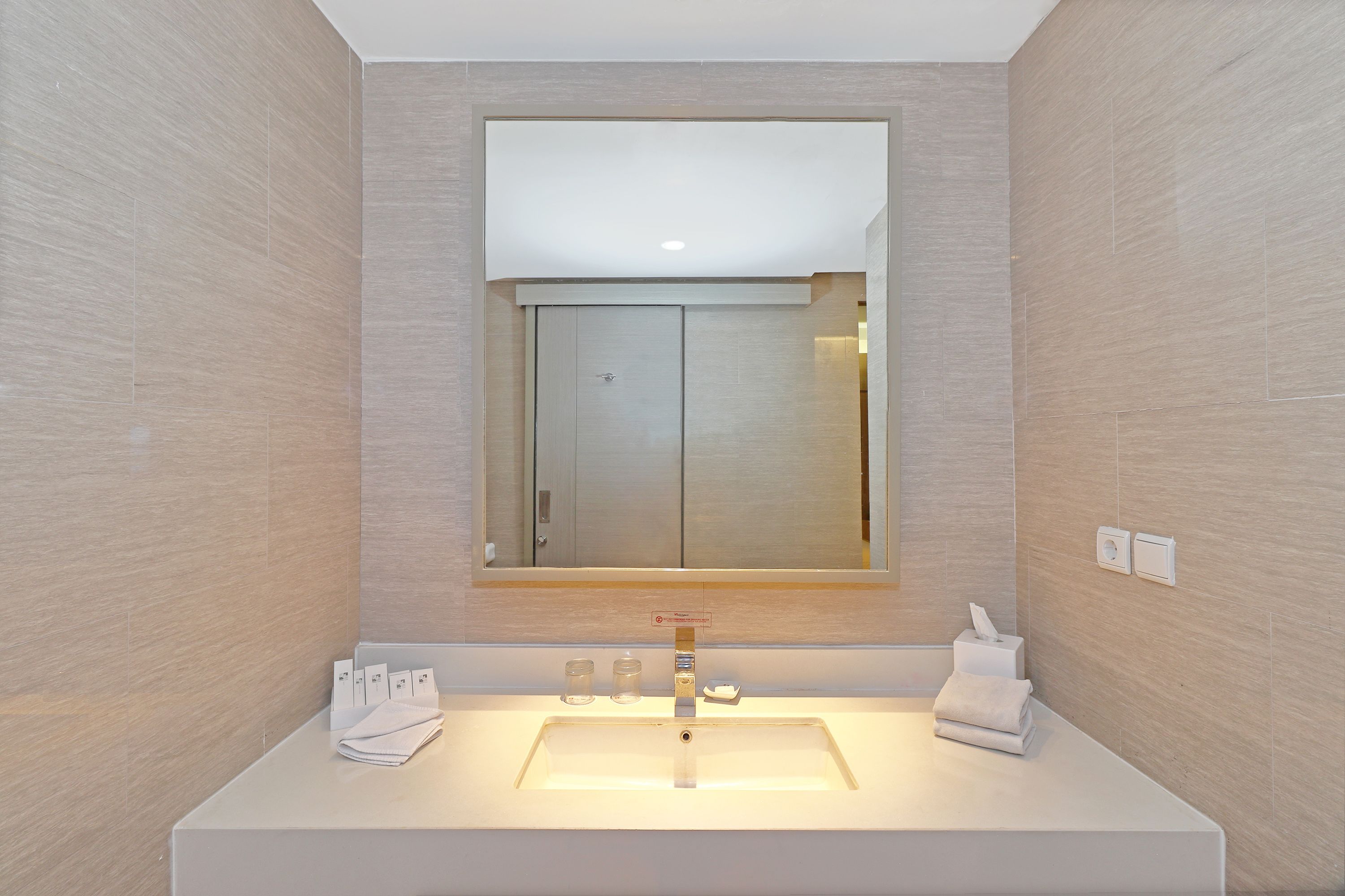 A modern bathroom with a large mirror, a white sink, and two towels.