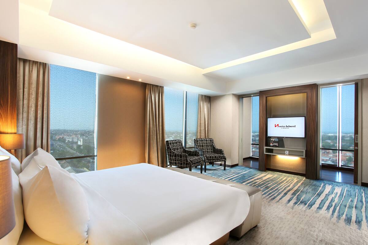 Una habitación de hotel con una cama grande, dos sillones, un televisor y vistas a la ciudad.