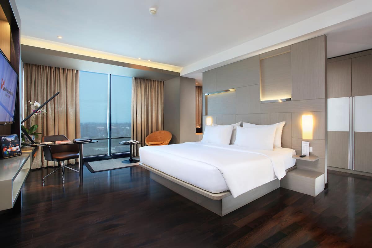 Una habitación de hotel moderna con una cama grande, un escritorio con silla, un televisor y vista a la ciudad.